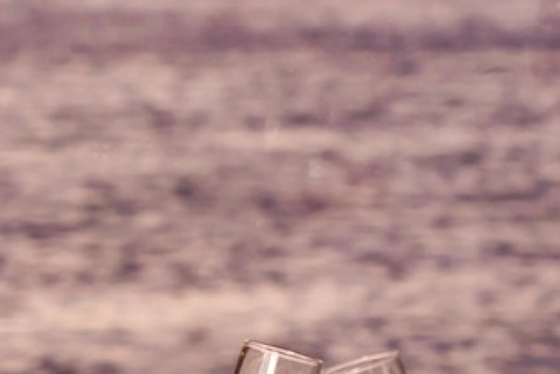 A couple clinking glasses at a candlelit dinner by a river, with a lit bridge in the background during sunset.