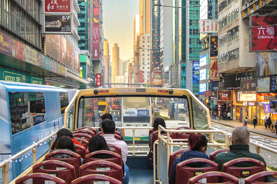 View from the upper deck of a double-decker bus in a busy urban area with tall buildings and traffic.