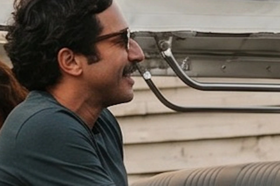 Two people shake hands beside a tuk-tuk styled vehicle with passengers, parked in front of a historic building.
