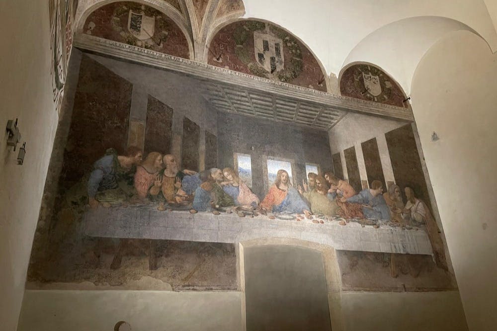 최후의 만찬에서 예수와 그의 제자들을 묘사한 프레스코화로, 아치와 장식 문장이 있는 어두운 방에 있습니다.