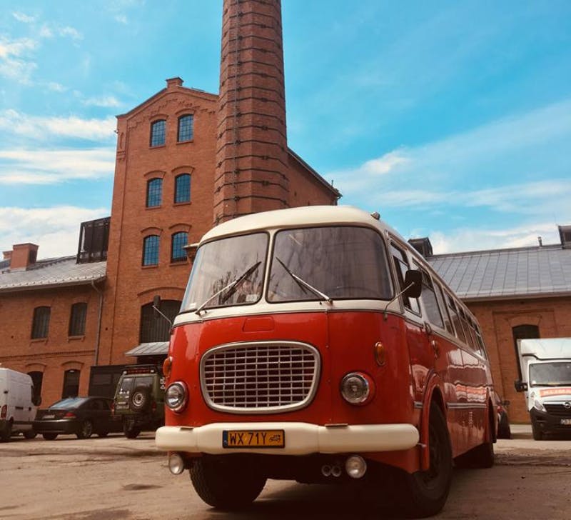 青空の下に背の高い煙突がある古いレンガ造りの建物の前には、ヴィンテージの赤と白のバスが停まっています。