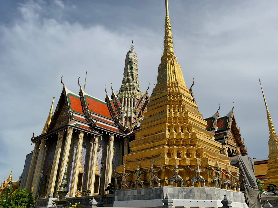 Golden stupa and ornate temple buildings with colorful roofs and intricate details under a cloudy sky.