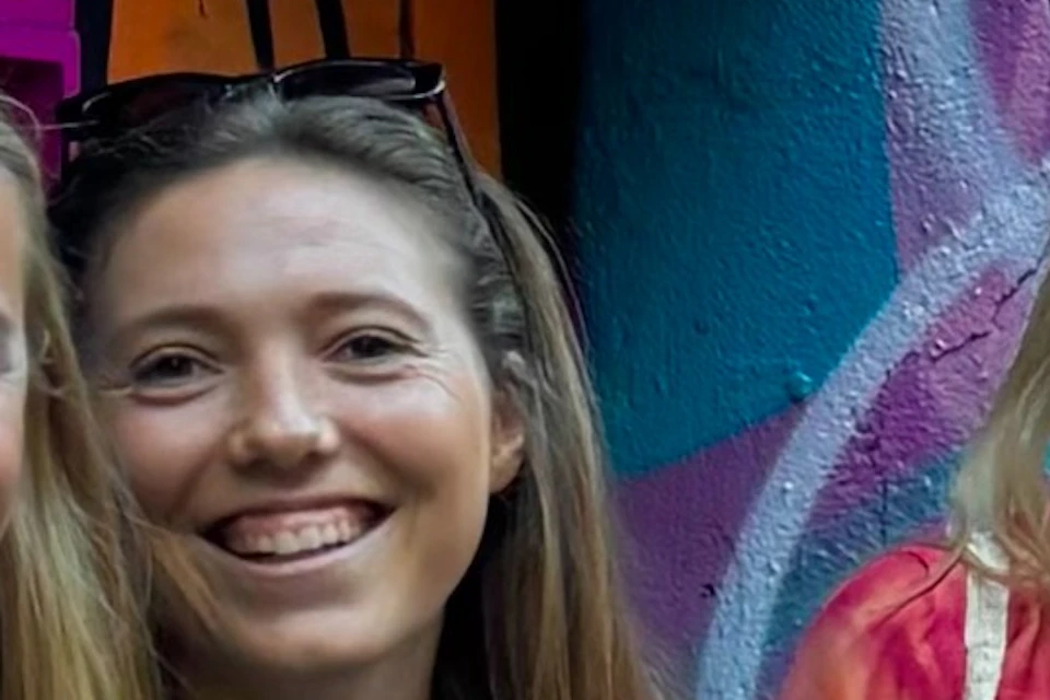 Three women standing together, smiling, in front of a colorful, graffiti-covered wall in an alleyway.
