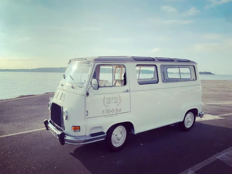 A white vintage van parked by a waterfront with "Le French Bus" written on the side.