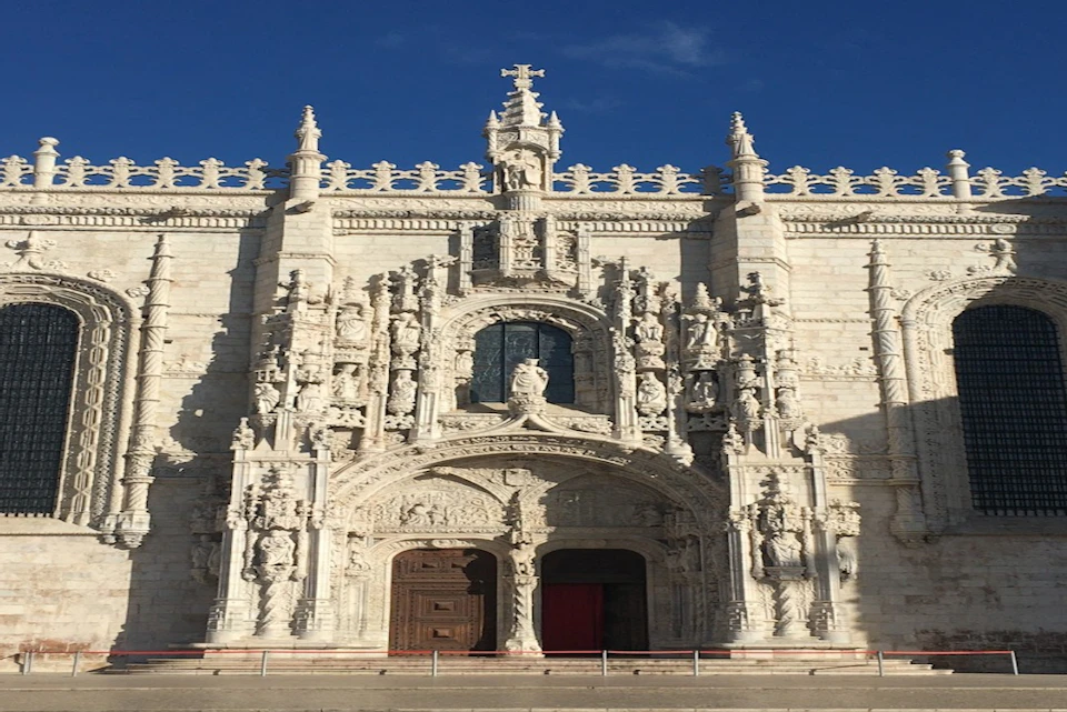 Ornate stone facade of a historical building with intricate carvings, statues, and a large wooden door, set against a clear blue sky.