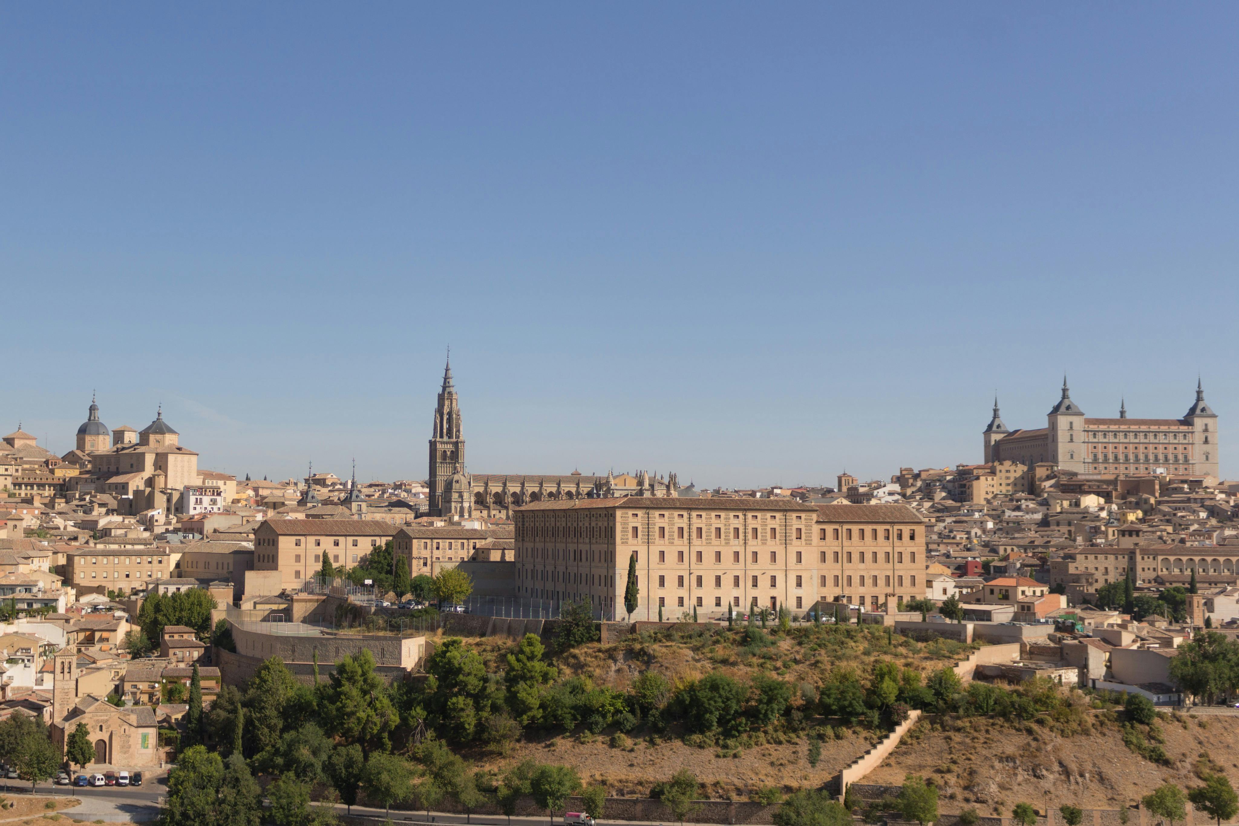 Un paysage urbain montrant des bâtiments historiques, dont une cathédrale avec une haute flèche, sous un ciel bleu clair.