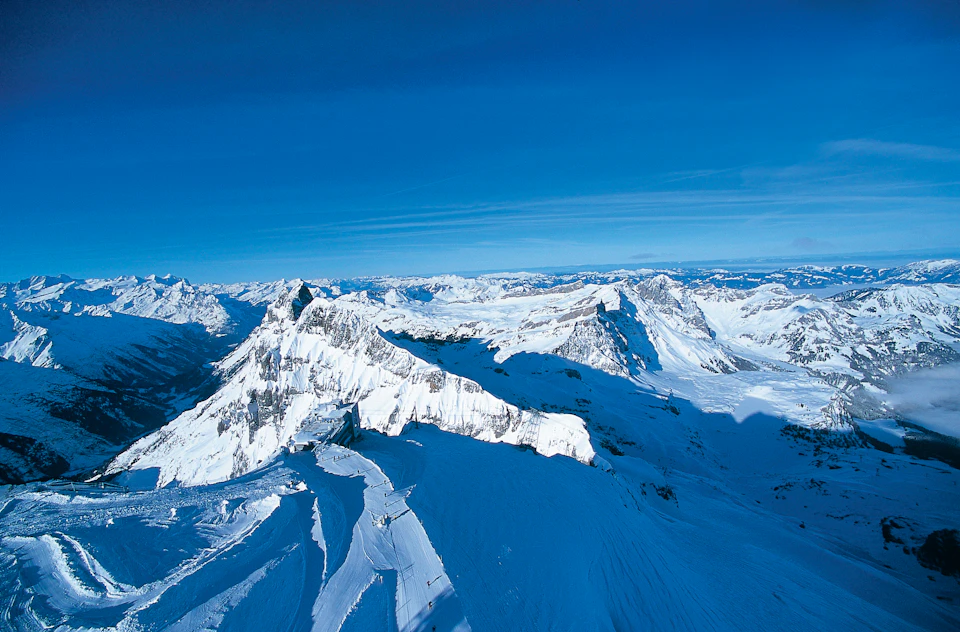 Snow-covered mountain range under a clear blue sky, displaying rugged peaks and deep valleys.