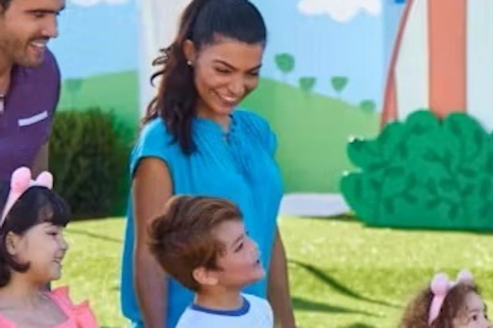 A family of four interacts with a costumed character in an outdoor play area with colorful decorations.