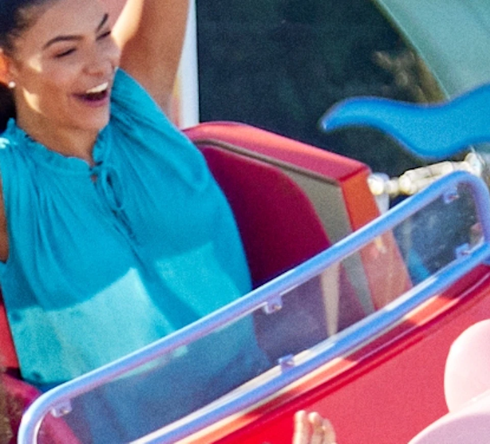 Children and adults ride a roller coaster with red cars shaped like Peppa Pig, against a backdrop of a house and colorful canopy.