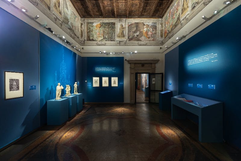 Una galleria presenta tre sculture astratte dai toni scuri montate su pareti chiare con soffitto in legno e illuminazione a faretti.