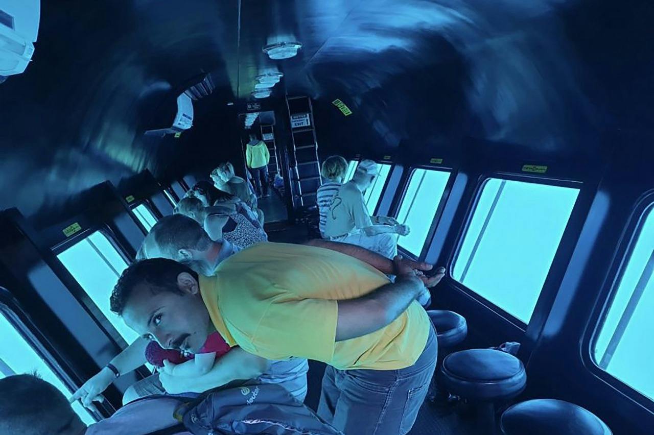 People inside a submarine-like vehicle looking out through large underwater windows, with a blue-lit interior.