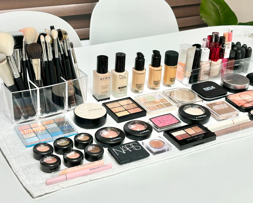 A neatly organized makeup collection on a table, including brushes, foundations, eyeshadows, and lip products.