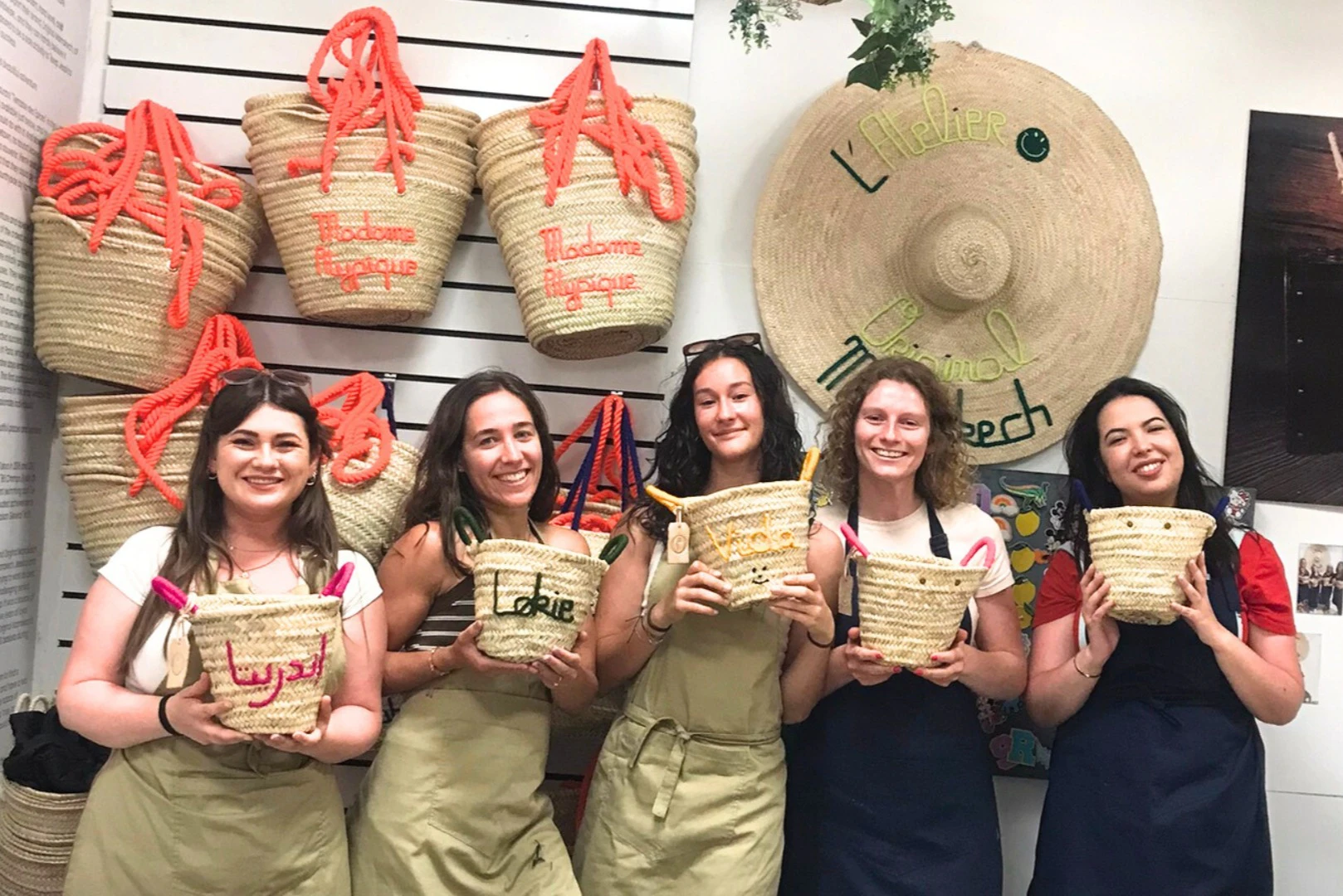 Five people standing in a row, each holding a woven basket bag, with more basket bags hanging on the wall behind them.