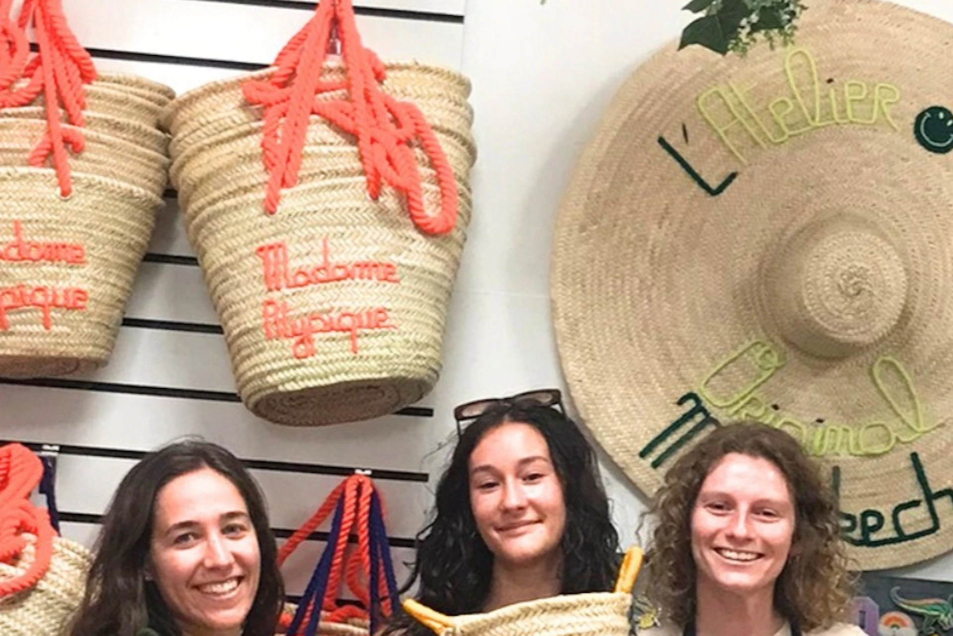 Five people standing in a row, each holding a woven basket bag, with more basket bags hanging on the wall behind them.