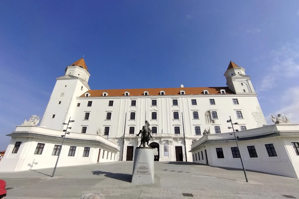 Large white castle with red roofs, four towers, and a courtyard centered by an equestrian statue, under a clear blue sky.