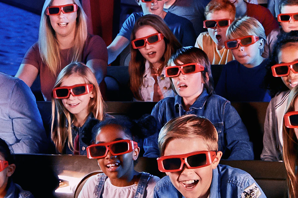 A group of people wearing 3D glasses sits in a theme park ride vehicle labeled "Far Far Away."