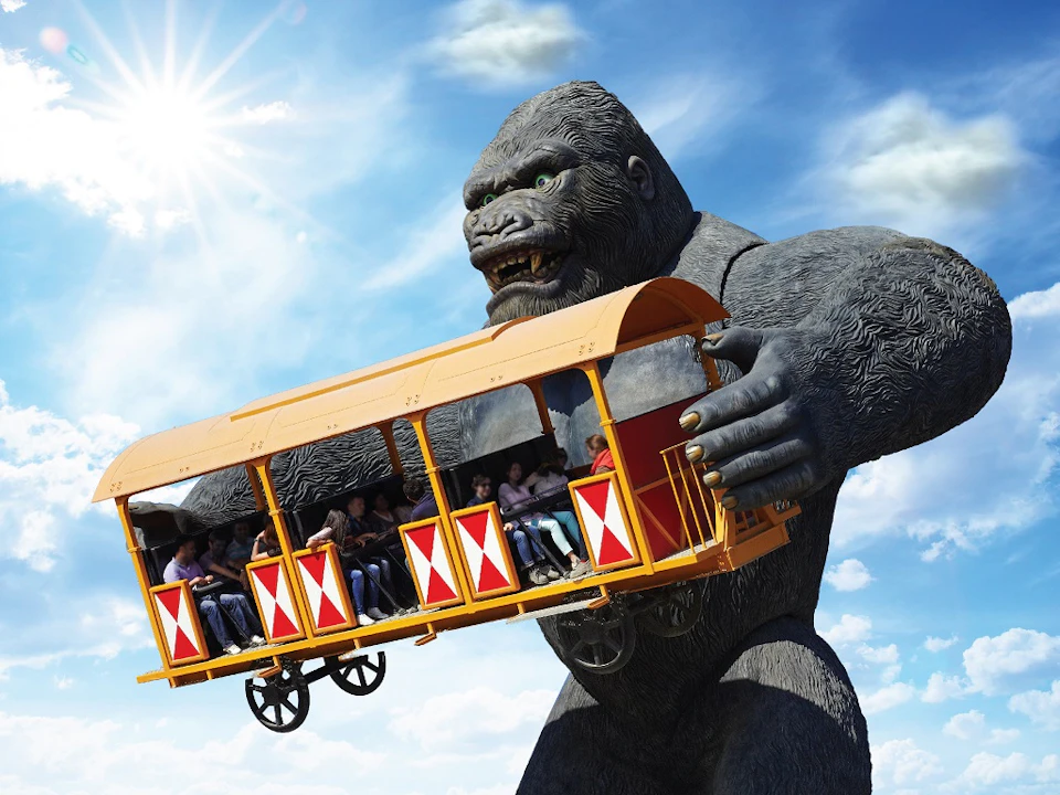 A giant gorilla statue holding a bright orange amusement park ride with people inside, set against a sunny, blue sky.