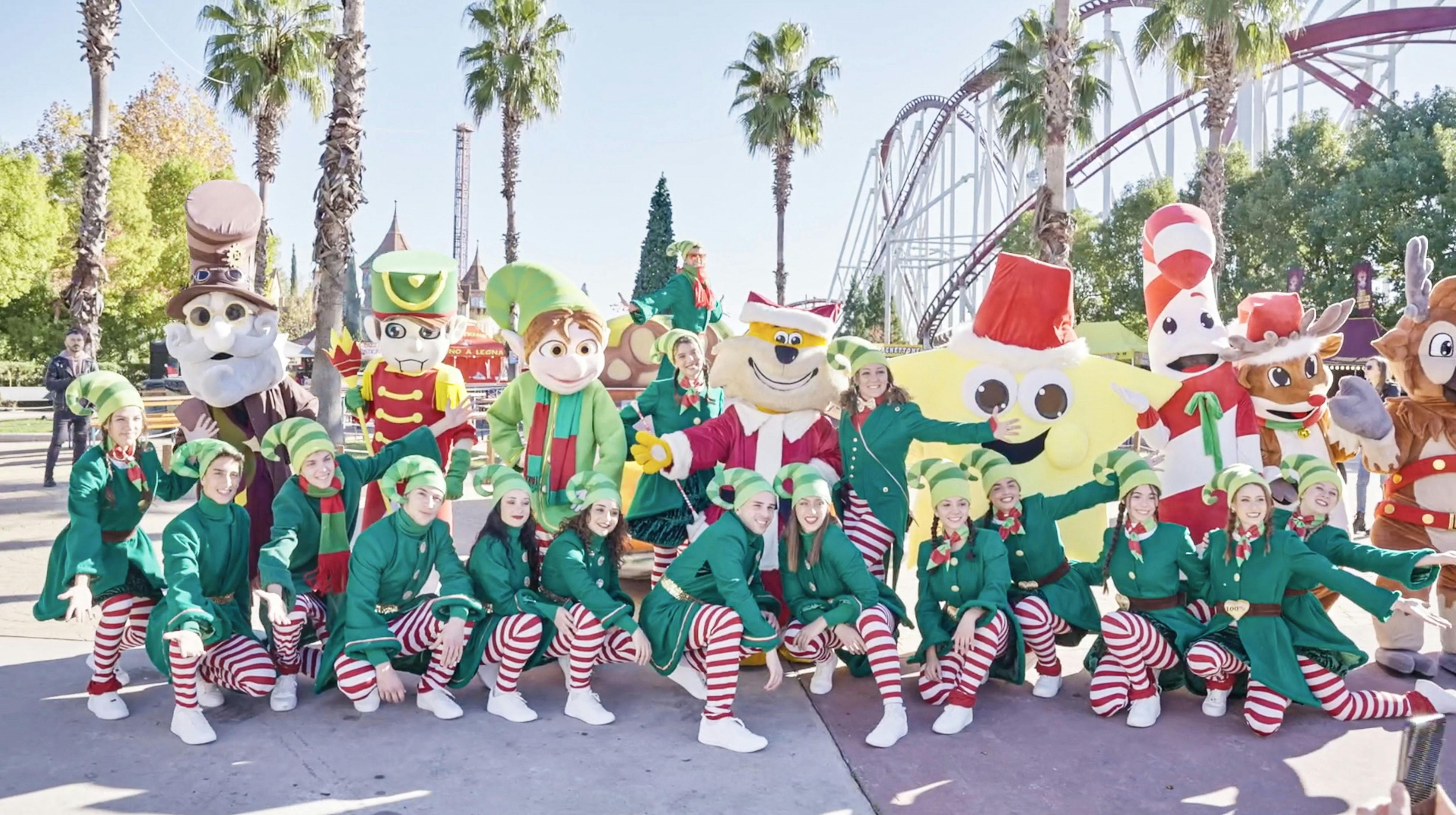 엘프와 마스코트를 포함한 축제 의상을 입은 사람들이 롤러코스터를 배경으로 포즈를 취하고 있습니다.