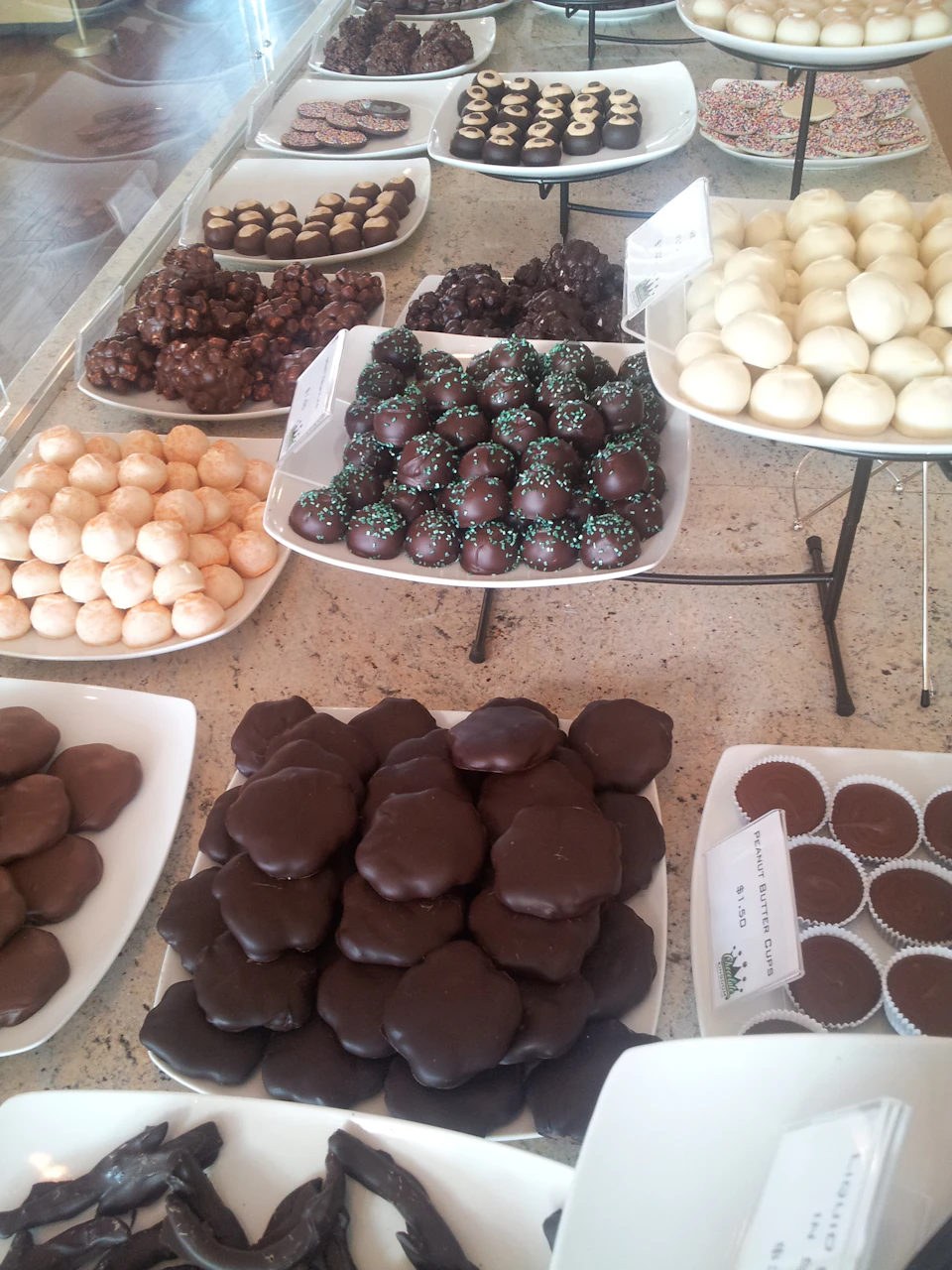 Assortment of various chocolates and truffles displayed on white plates atop a countertop.