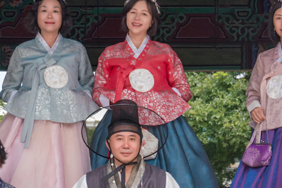 A group of people wearing traditional Korean hanbok standing in front of an ornately decorated structure.