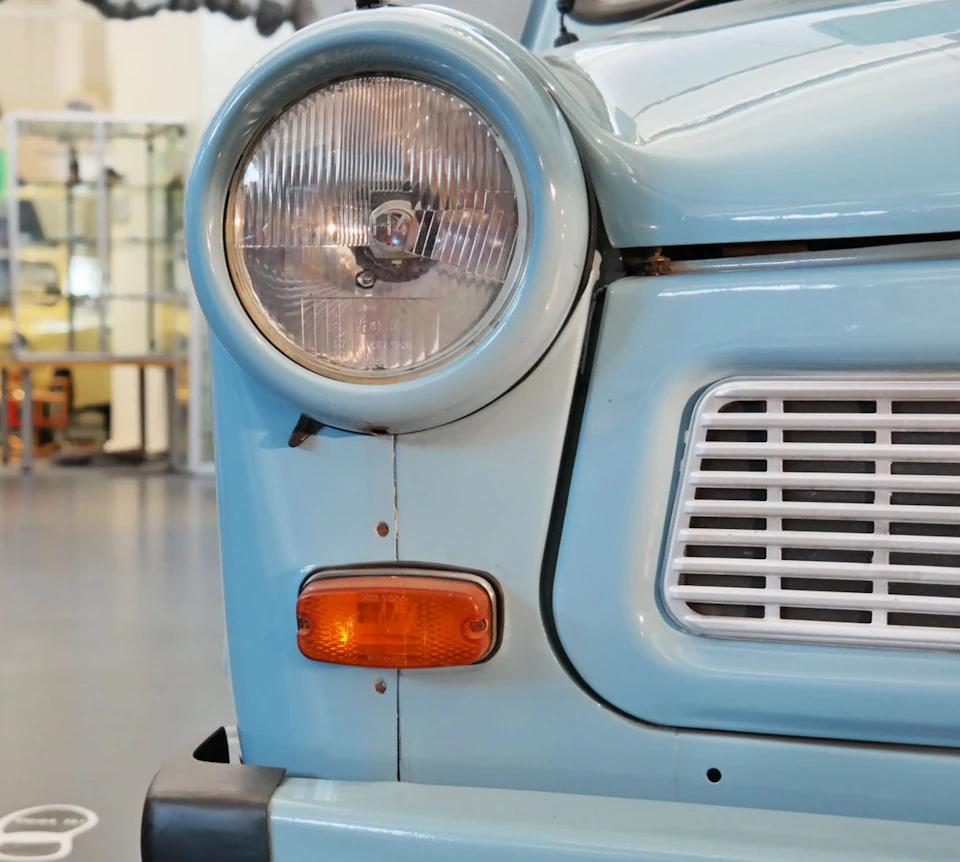 Close-up of the front left headlight and grille of a vintage light blue car with an orange side marker light.