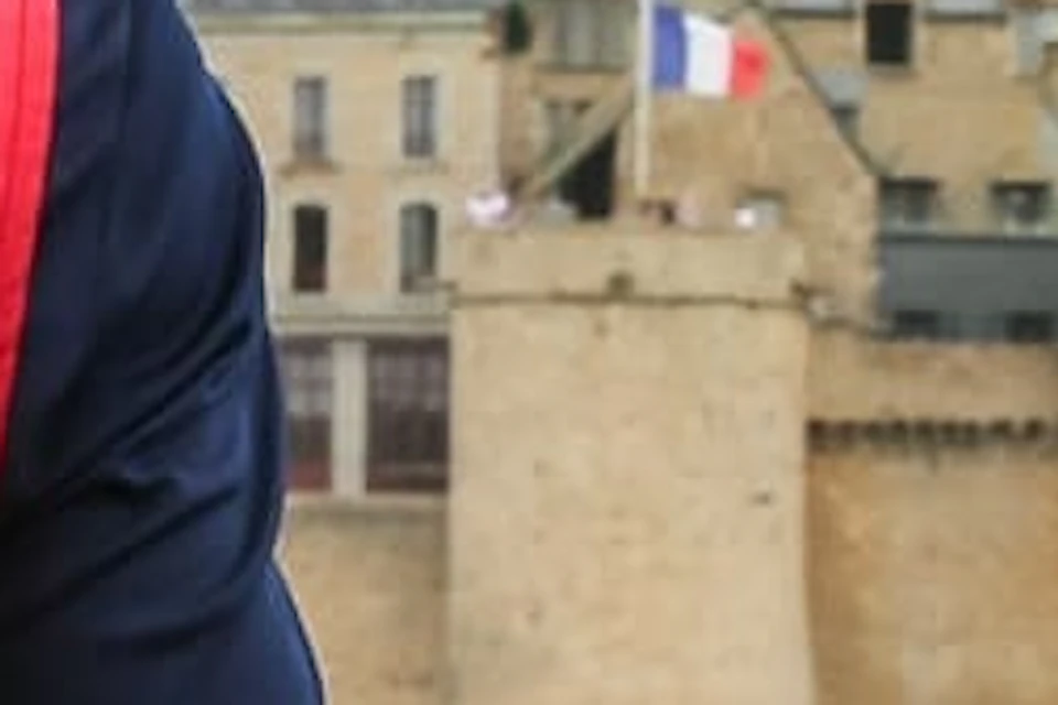 Two people stand on a bridge overlooking Mont Saint-Michel; one wears a red "Paris City Vision" vest.
