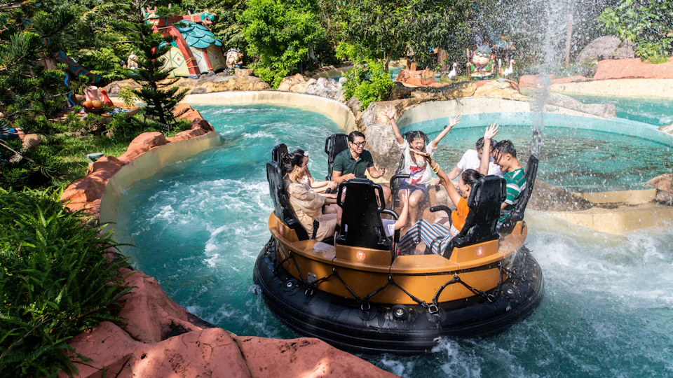 A group of people enjoying a water ride in a circular raft surrounded by flowing water and greenery on a sunny day.