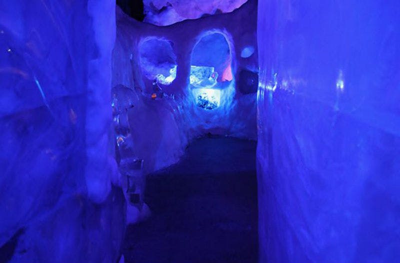 Narrow, dimly lit passageway with ice-covered walls and blue lighting. Small arches and alcoves are visible along the sides.