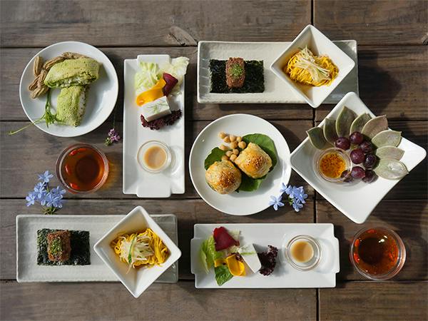 A table set with various plated dishes including pastries, salads, fruits, and tea, arranged neatly on a wooden surface.