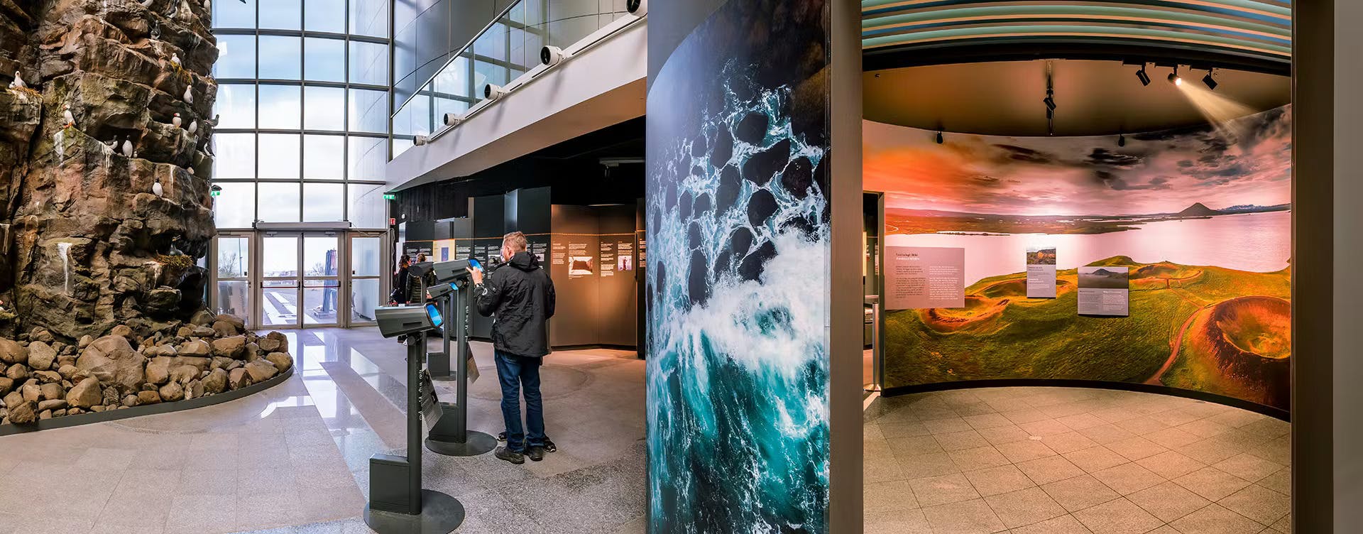 Et indendørs museum udstiller med informationspaneler, et stort havbølgebillede og en person, der interagerer med en skærm.