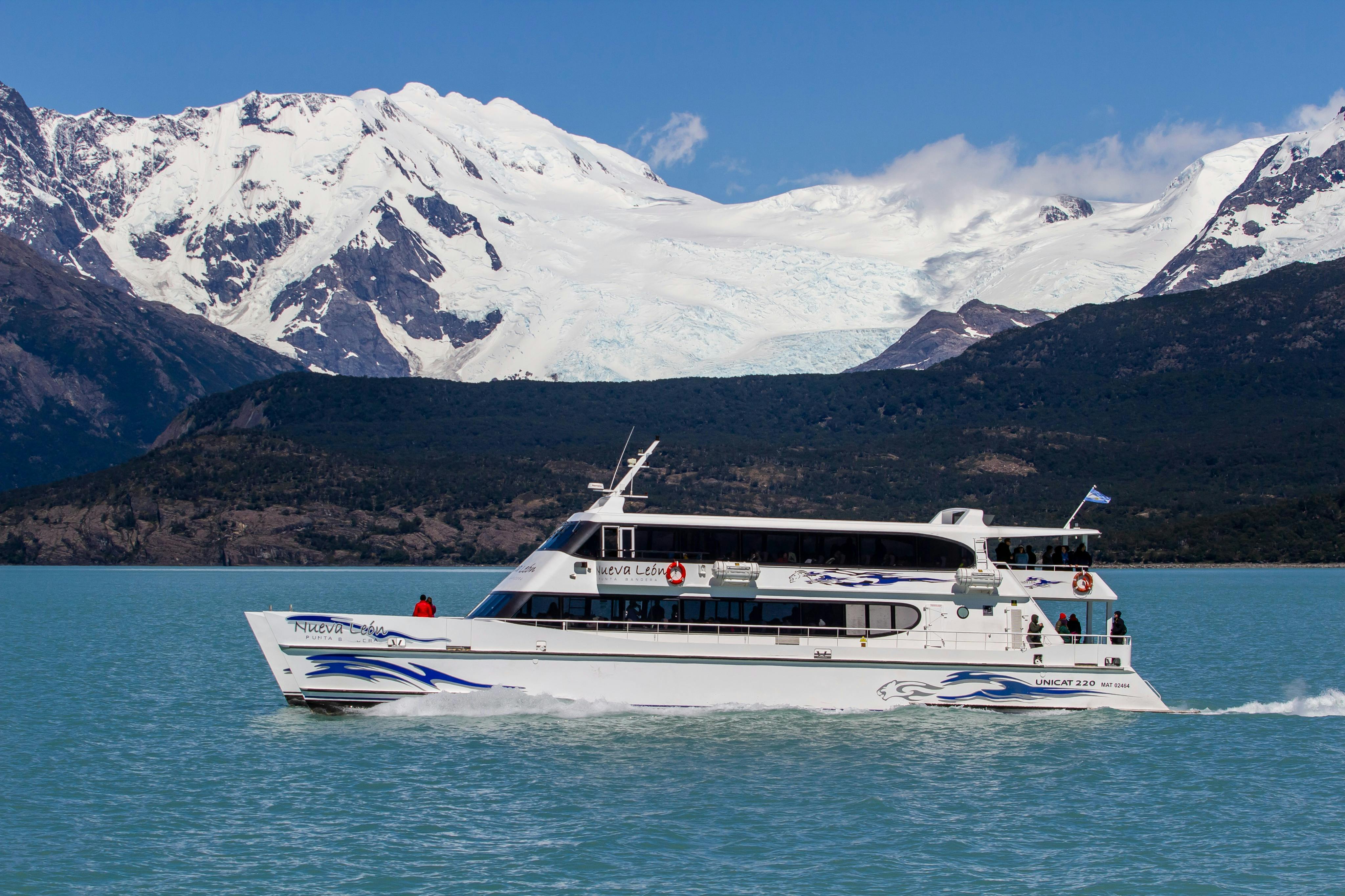 A white tour boat on a blue lake with snow-capped mountains and a glacier in the background under a clear sky.