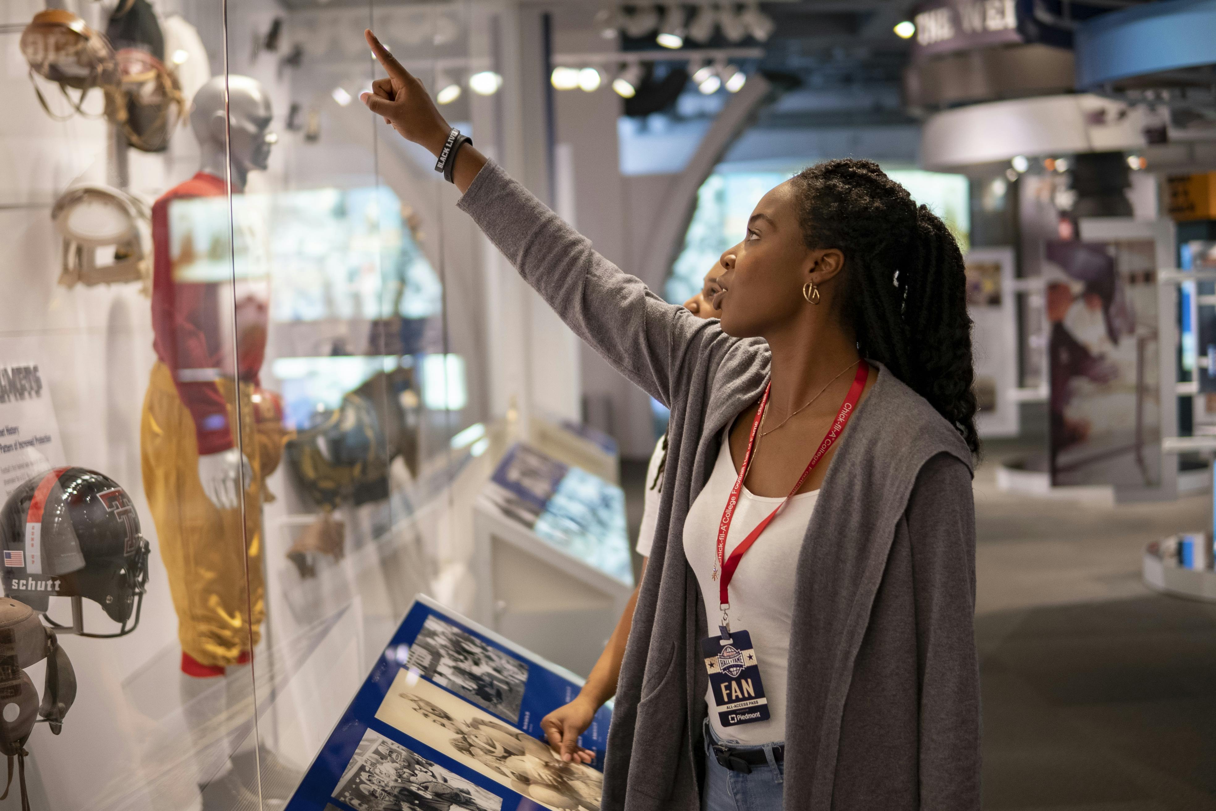 Osoba s odznakem „VĚJÍŘ“ ukazuje na exponát v muzeu a zabývá se vystavenými fotografiemi a artefakty.