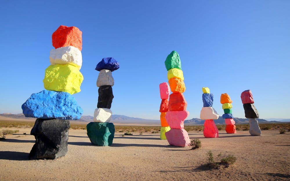 맑고 푸른 하늘 아래 사막 풍경 속에 다양한 색상의 밝게 칠해진 바위가 높이 쌓여 있습니다.