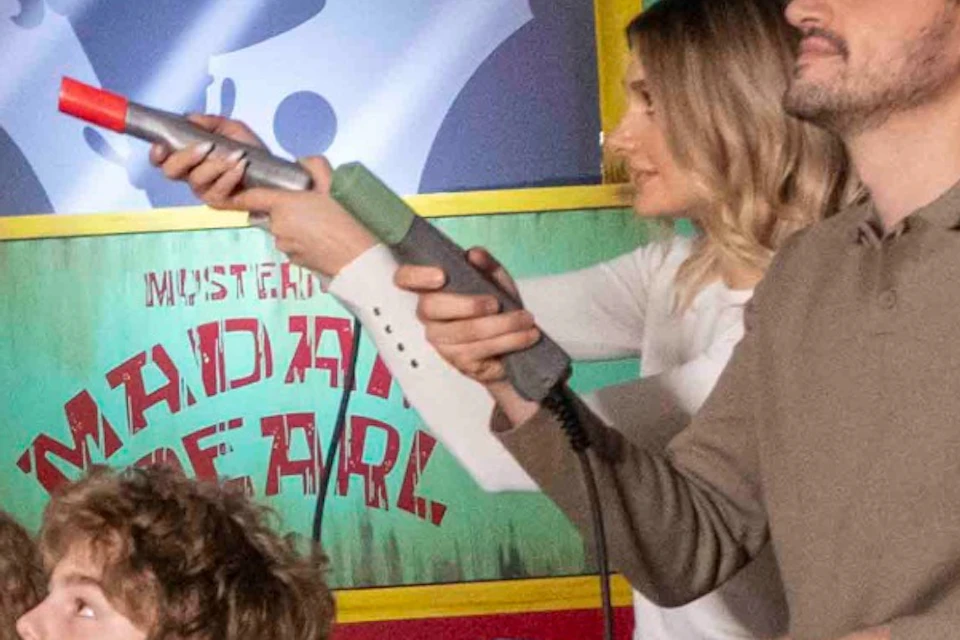 Two people in a themed ride vehicle aiming toy guns in an underwater-themed amusement park setting.