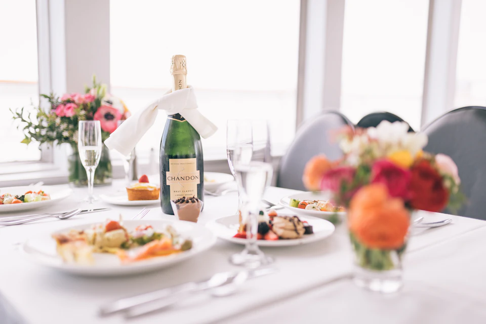 Dining table with plates of food, a bottle of Chandon champagne, wine glasses, and a bouquet of colorful flowers.