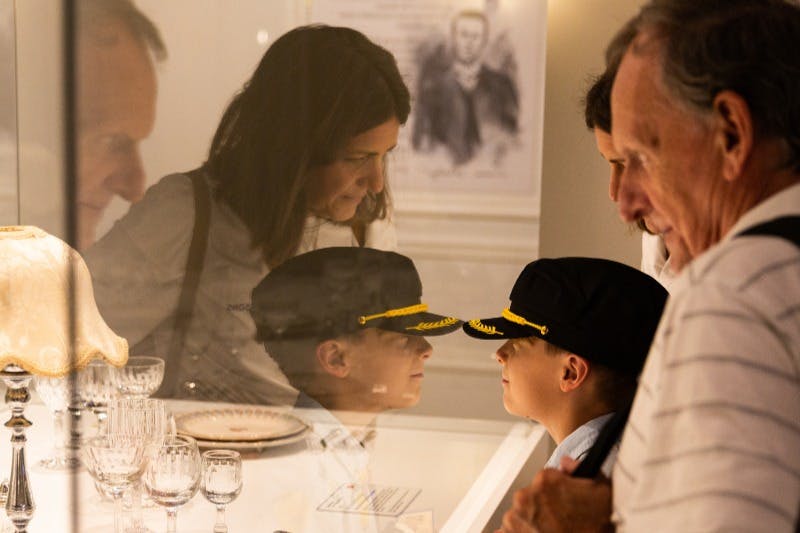 一个戴着制服帽子的男孩看着陈列柜。 三个成年人观察，背景中可以看到一幅历史肖像。