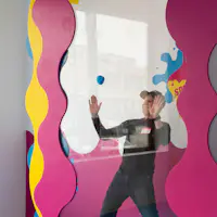 Una persona con un cappello premuto contro un vetro colorato con accenti ondulati gialli e rosa.