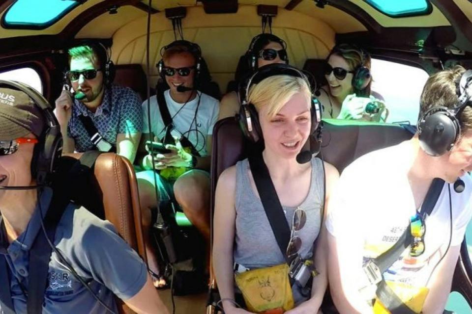 Six people wearing headsets seated inside a helicopter, smiling and interacting during the flight.