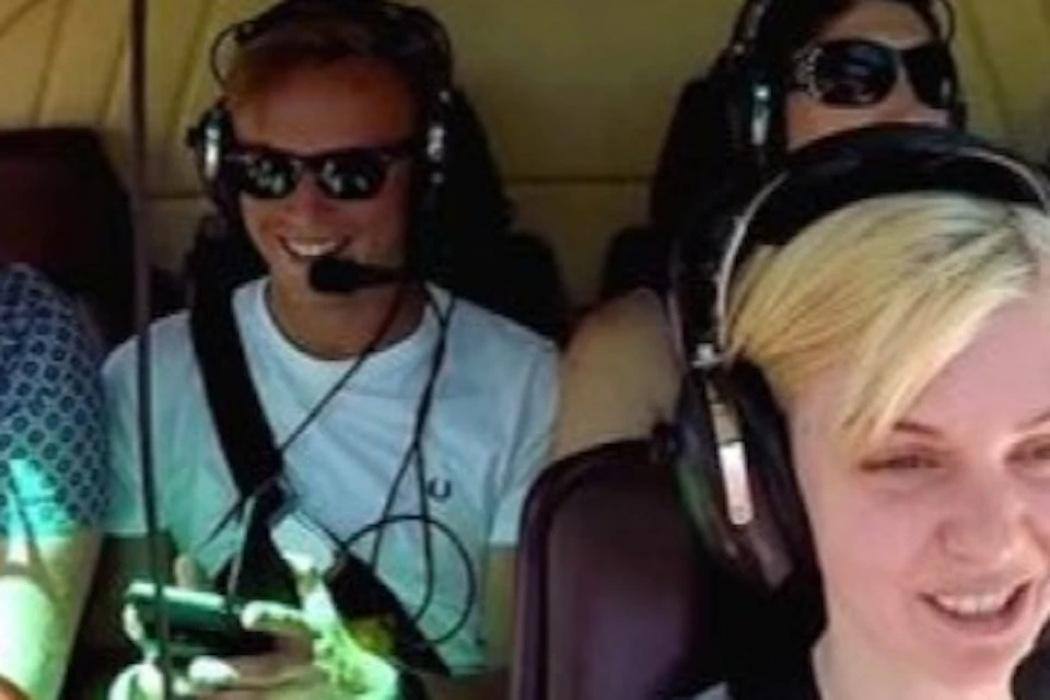 Six people wearing headsets seated inside a helicopter, smiling and interacting during the flight.