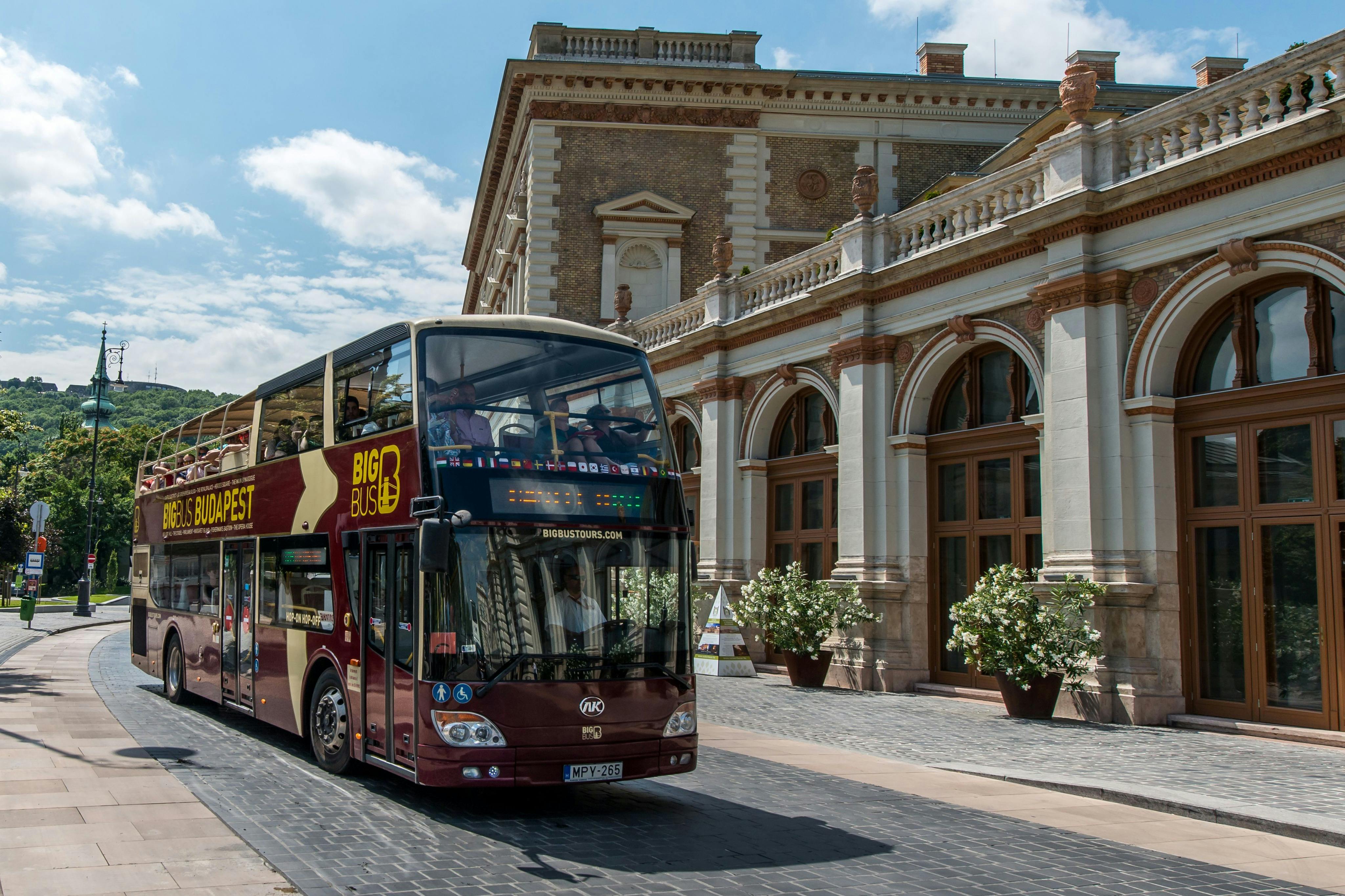 Um autocarro turístico vermelho de dois andares com a etiqueta "Big Bus Tours" está estacionado perto de um edifício histórico com janelas e colunas em arco.