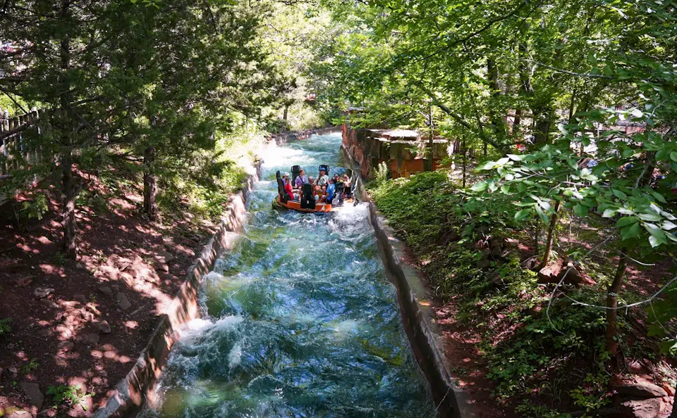 People riding a circular raft on a winding water rapids ride surrounded by lush green trees and foliage.
