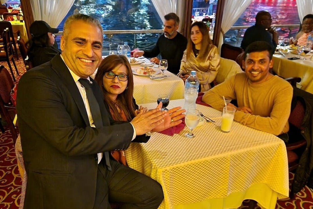 レストランのテーブルに5人が座り、笑顔で会話をしながら、窓から水の景色を眺めています。