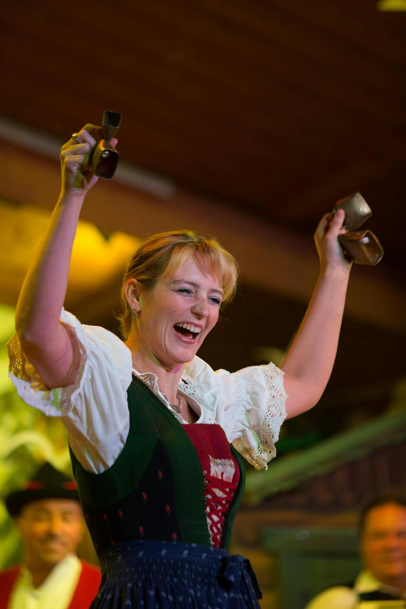 전통 바바리안 복장을 한 여성이 카우벨을 기운차게 들어올리고, 사람들은 뒤에서 미소를 짓고 있습니다.