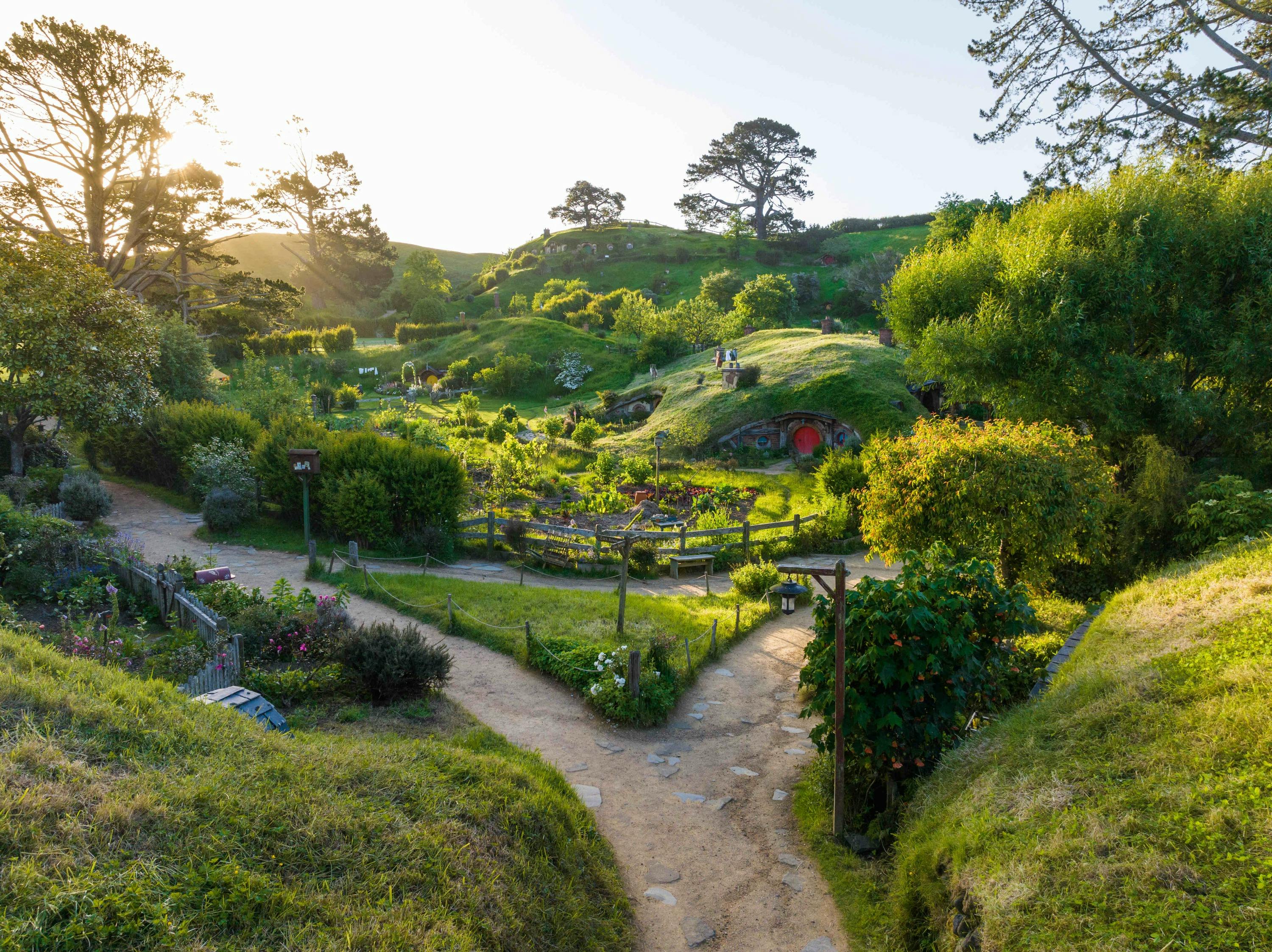 A scenic view of a lush green landscape with small hills, gardens, and a house with a round door embedded in a hillside.