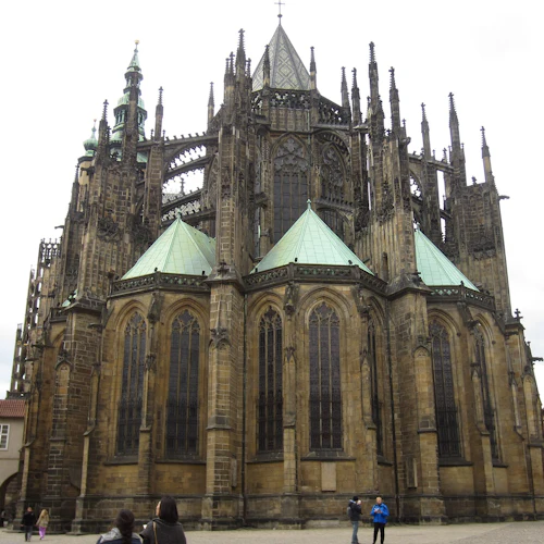 En stor gotisk katedral med invecklad arkitektur och gröna koppartak. Folk går runt dess bas.