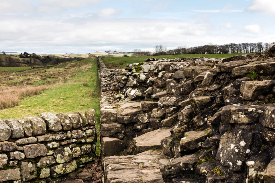 Ancient stone wall extending into the distance, surrounded by grassy fields and a partly cloudy sky.