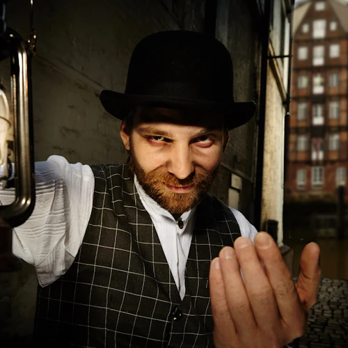 Man i rutig väst och bowlerhatt håller lyktan, stående i en smal gränd. Byggnader syns i bakgrunden.