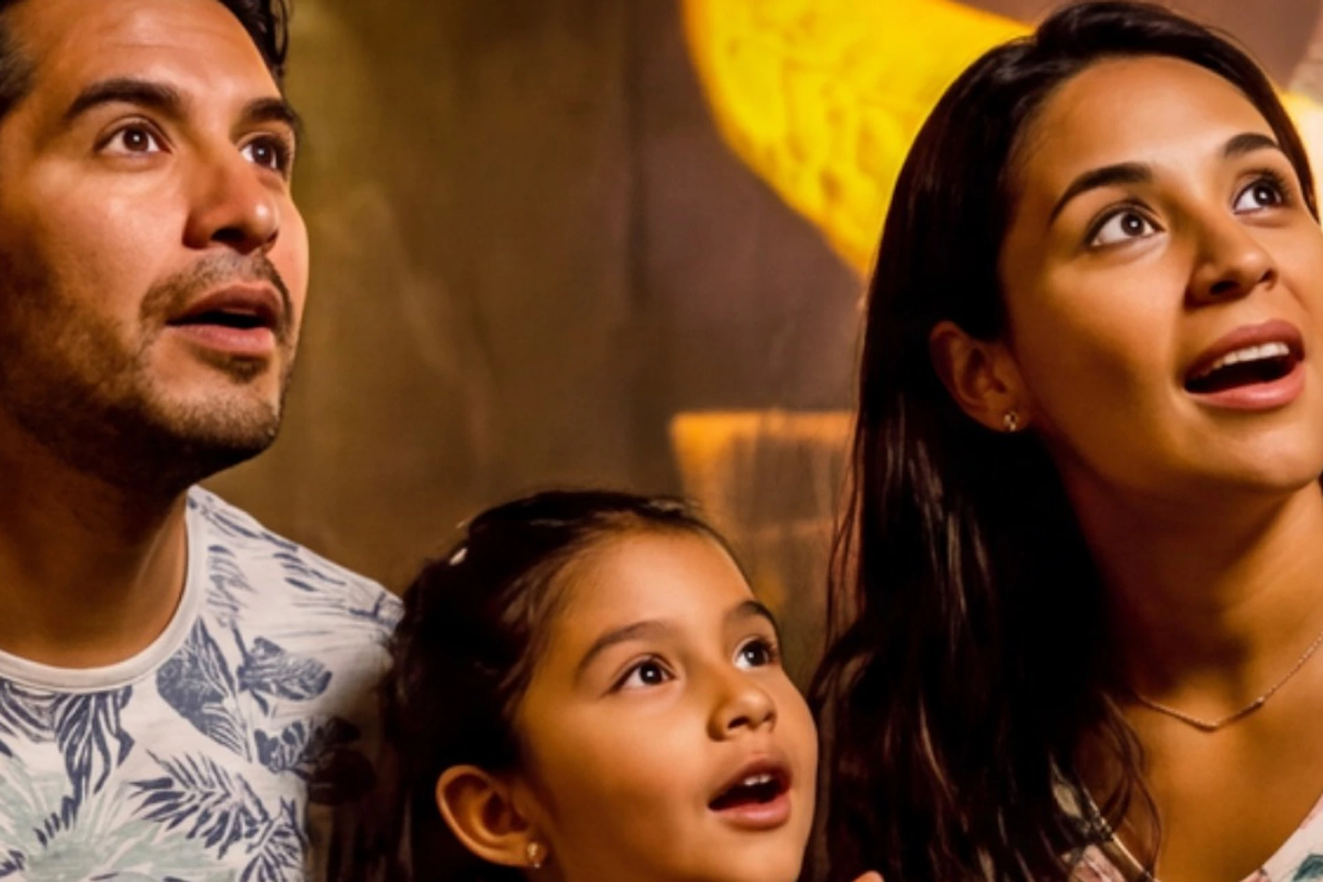 A family of three sitting indoors, looking amazed at an illuminated display of a historical painting in the background.