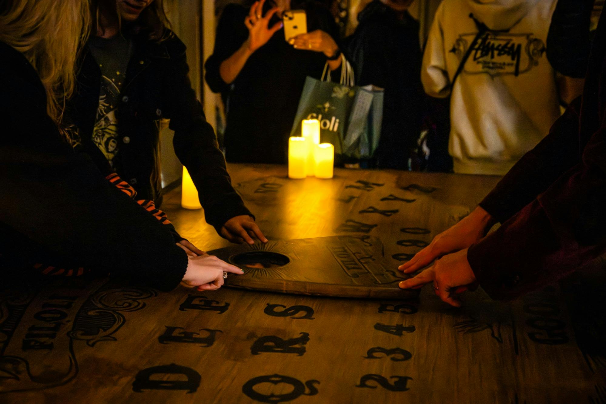 Οι άνθρωποι χρησιμοποιούν έναν πίνακα Ouija σε ένα τραπέζι με ορατά κεριά, γράμματα και αριθμούς.