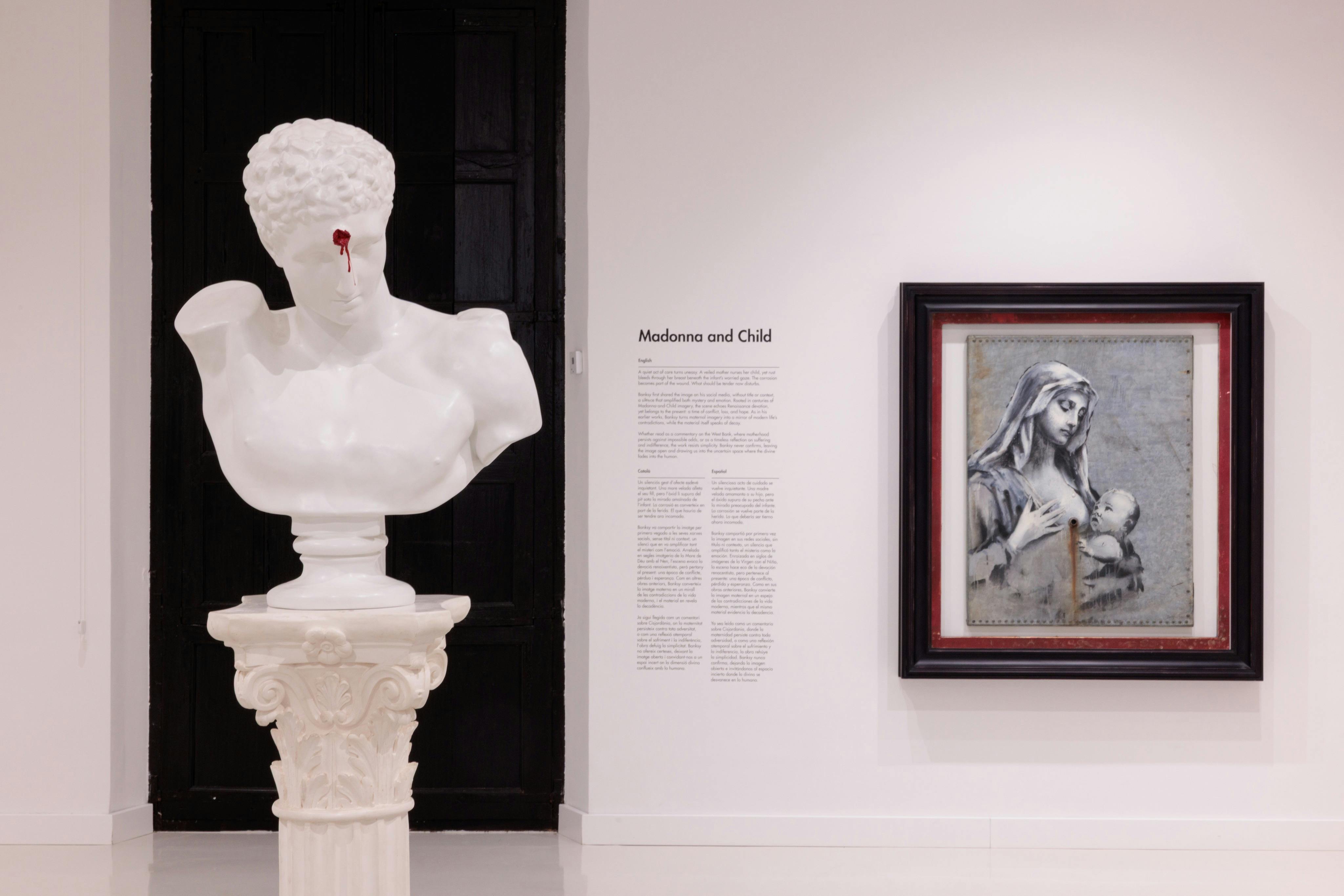 '마돈나와 아이' 라고 적힌 벽에 문구가 적힌 갤러리에 전시된 장식용 받침대에 새겨진 하얀 대리석 흉상 동상.